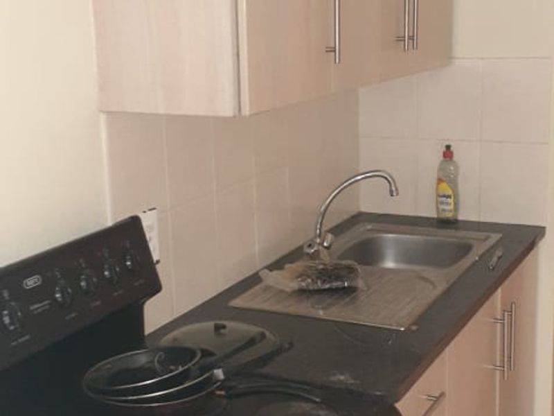 A compact kitchen featuring light-toned laminate cabinetry, a stainless steel sink with mixer tap, tiled splashback, and a freestanding stove.