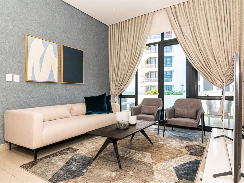 Modern living room featuring tiled flooring, textured feature wall, and large sliding glass doors providing access to the balcony.