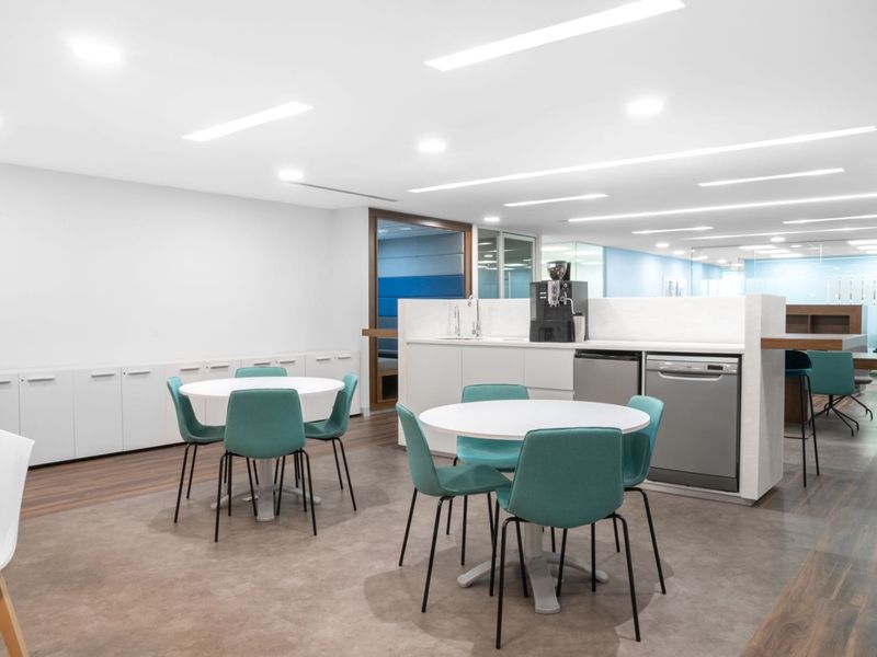 Modern open-plan office break area featuring a functional kitchenette with built-in cabinetry, integrated dishwasher, and recessed ceiling lighting.