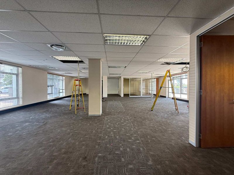 Open-plan office space featuring suspended ceilings, carpet tiles, and glass partitions, currently undergoing maintenance with some ceiling tiles removed.