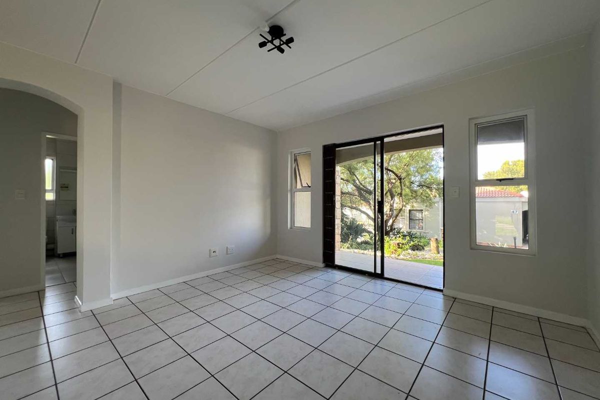 A bright, empty living area featuring tiled flooring, a modern ceiling light, and sliding glass doors that open onto a patio.