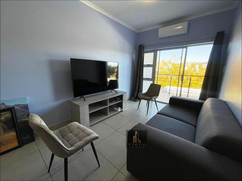 A well-lit living room featuring tiled flooring, a wall-mounted air conditioning unit, and large sliding glass doors providing access to a balcony.