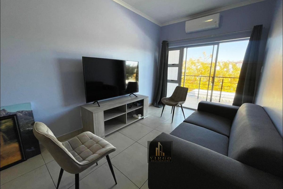 A well-lit living room featuring tiled flooring, a wall-mounted air conditioning unit, and large sliding glass doors providing access to a balcony.