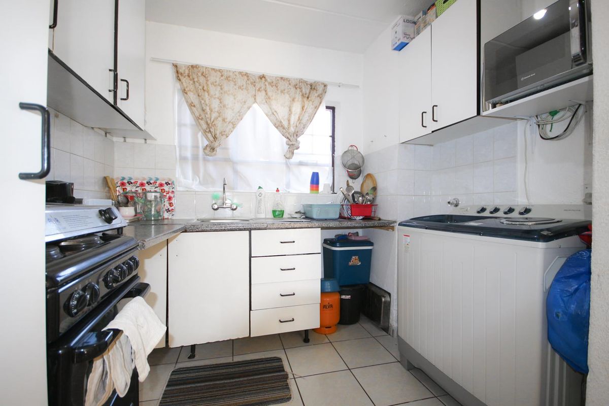 Compact kitchen featuring white cabinetry, tiled splashbacks, a freestanding stove, and dedicated space for a top-loading washing machine.