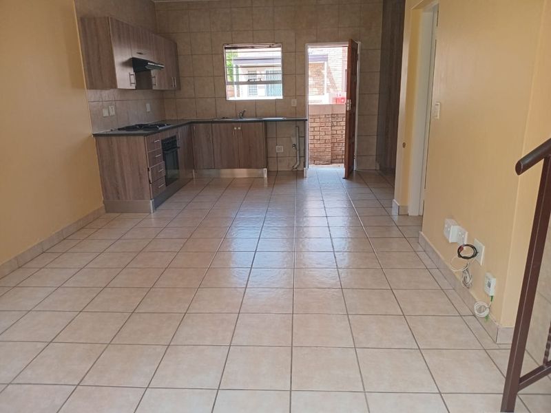 Open-plan kitchen and living area featuring tiled flooring, built-in cabinetry with integrated appliances, and direct access to an outdoor space.