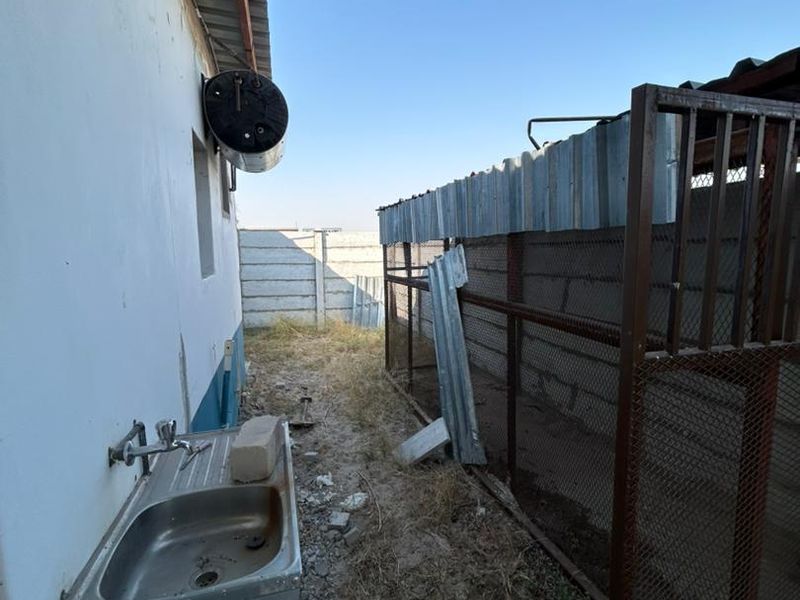 Rear exterior area featuring an external sink, wall-mounted electric geyser, and metal enclosure structure with precast concrete boundary walling.