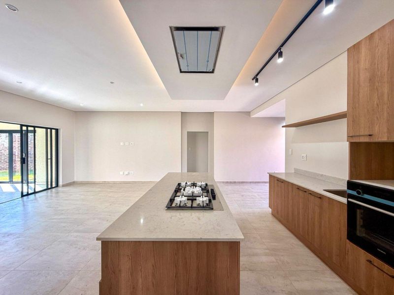 Modern open-plan kitchen and living area featuring a central island with gas hob, built-in oven, stone countertops, and sleek wood cabinetry.