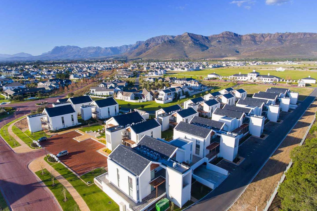 An aerial view of a modern residential estate featuring contemporary homes with pitched roofs, paved driveways, and well-maintained green spaces against a mountain backdrop.