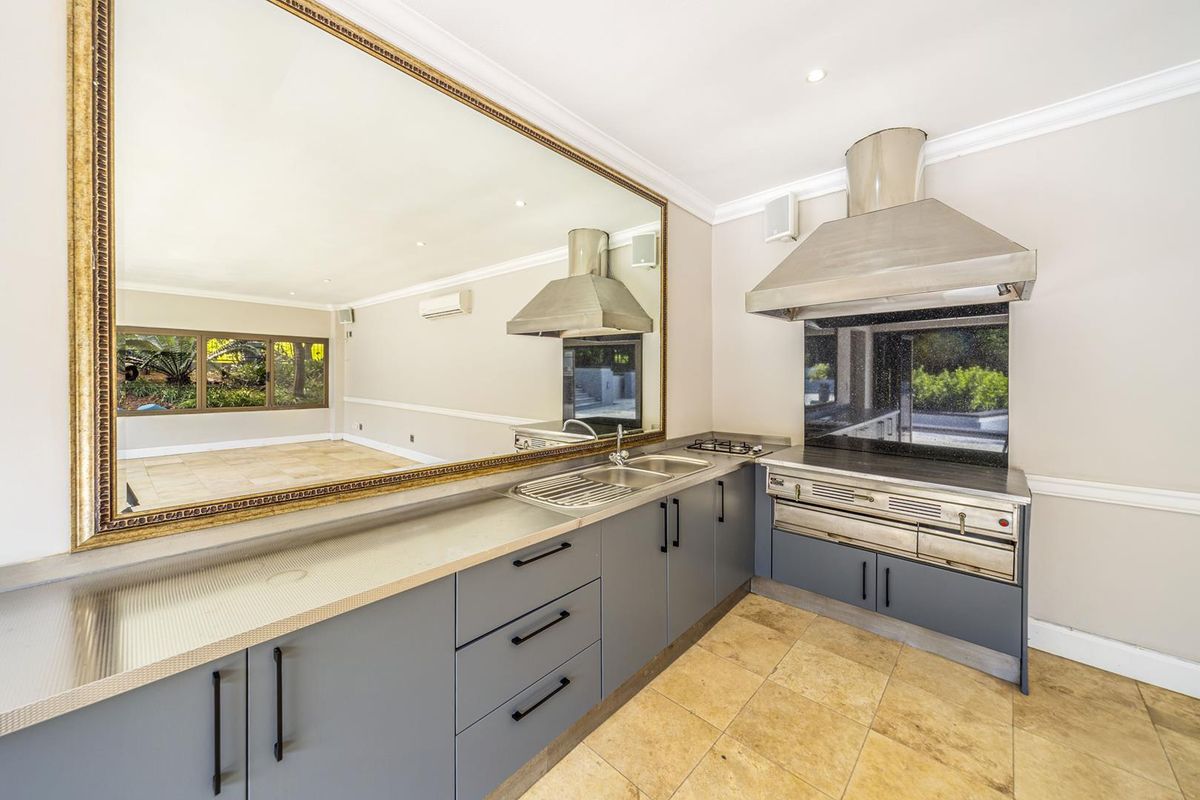 Modern kitchen featuring grey cabinetry, stainless steel extractor fan, built-in stove, and stone-tiled flooring, complemented by a large wall-mounted mirror.