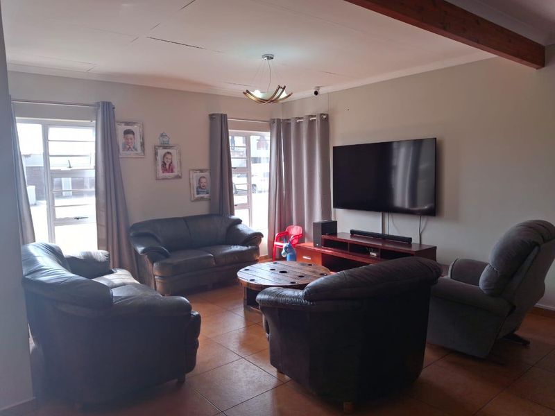 A comfortable living room featuring tiled flooring, an exposed timber ceiling beam, and natural light through aluminium-framed windows.