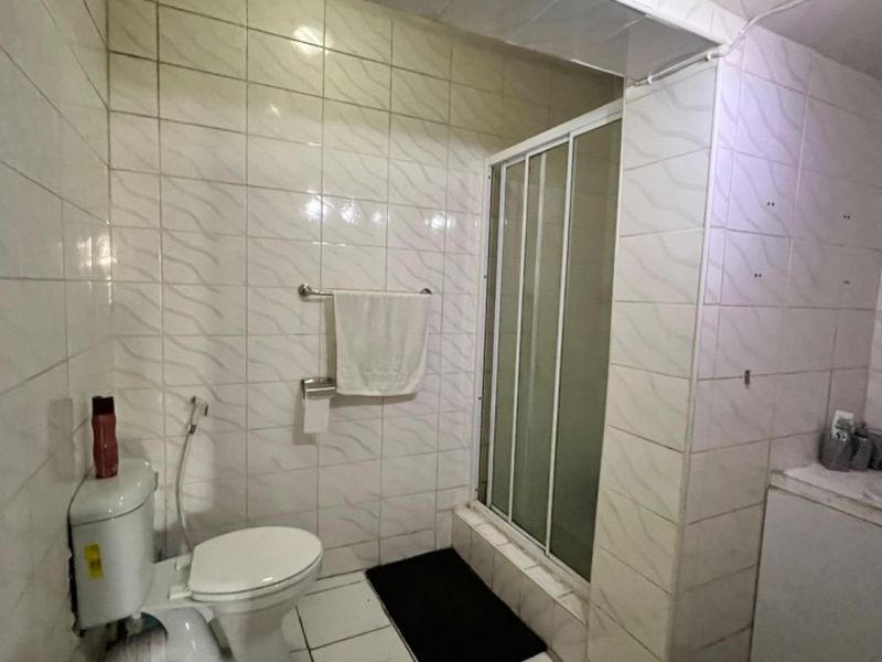 A functional bathroom featuring a shower enclosure, toilet, and vanity unit with a washbasin, finished with wall tiling.