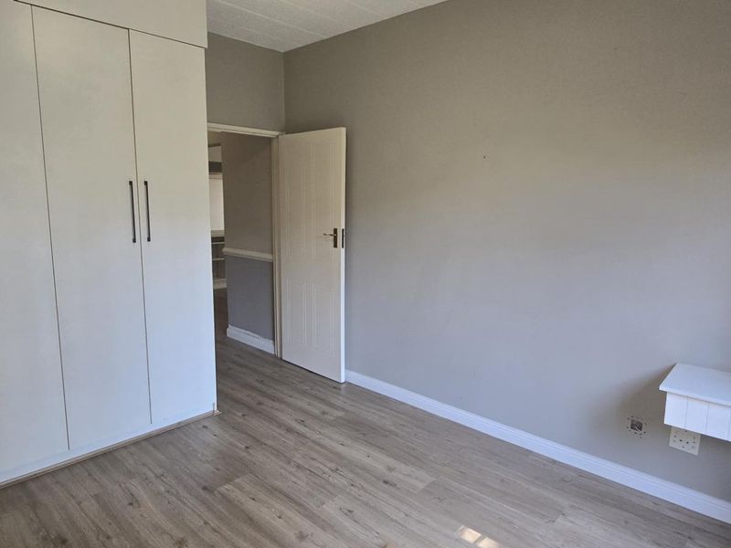 A clean, empty bedroom featuring neutral grey walls, light wood-look laminate flooring, and ample built-in cupboard storage.