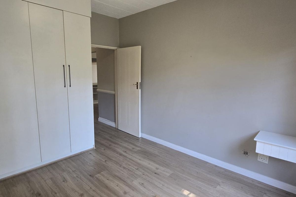 A clean, empty bedroom featuring neutral grey walls, light wood-look laminate flooring, and ample built-in cupboard storage.