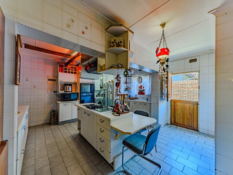 A dated kitchen featuring built-in cabinetry, a central island with a gas hob, tiled surfaces throughout, and a stable door leading to the exterior.
