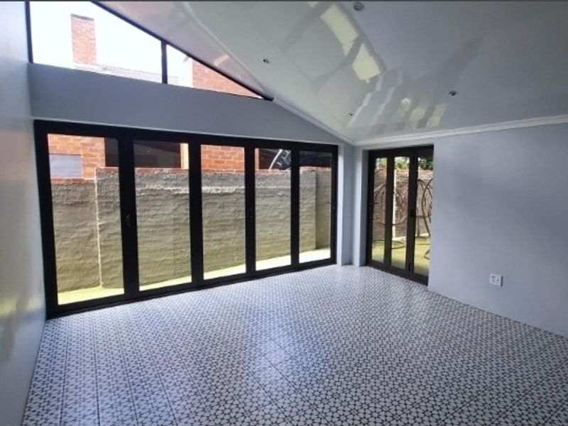 A bright, modern living space featuring patterned tiled flooring, a pitched ceiling with recessed lighting, and large bi-fold doors opening to the exterior.