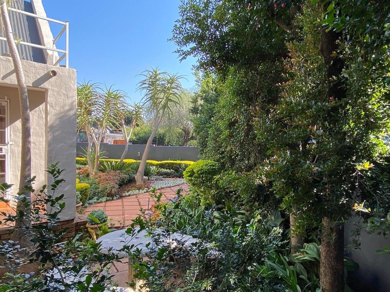 A well-maintained garden area featuring mature landscaping, established trees, and a paved walkway adjacent to the office building exterior.