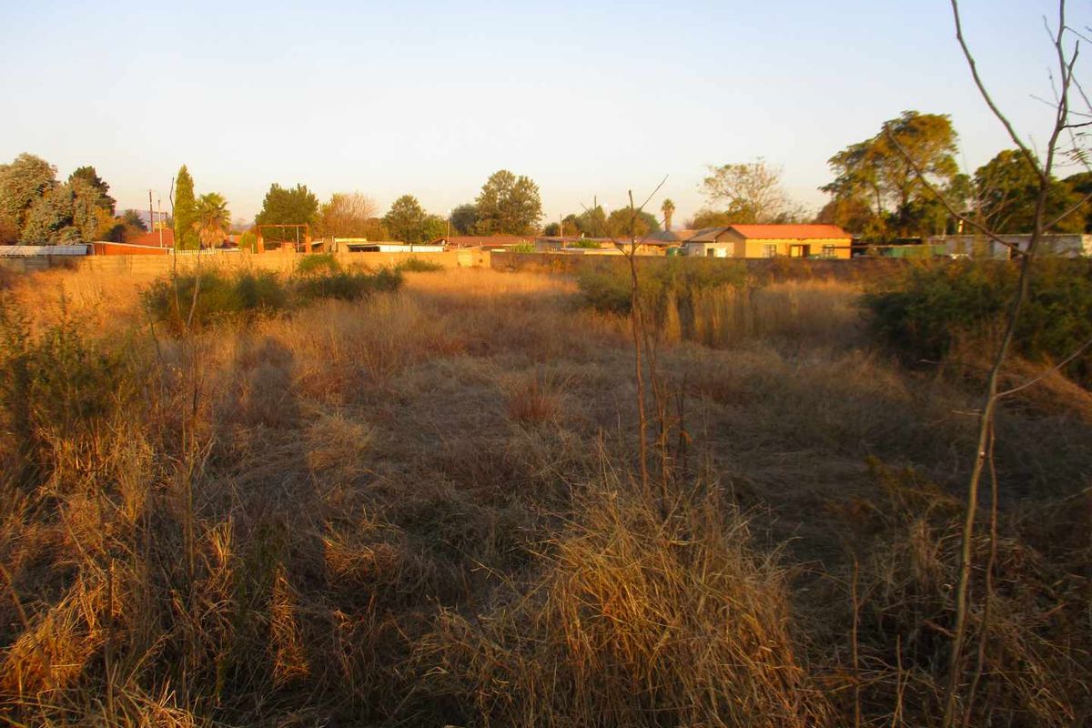 A vacant residential plot featuring dry grass and a perimeter wall, offering a clear space for potential development.