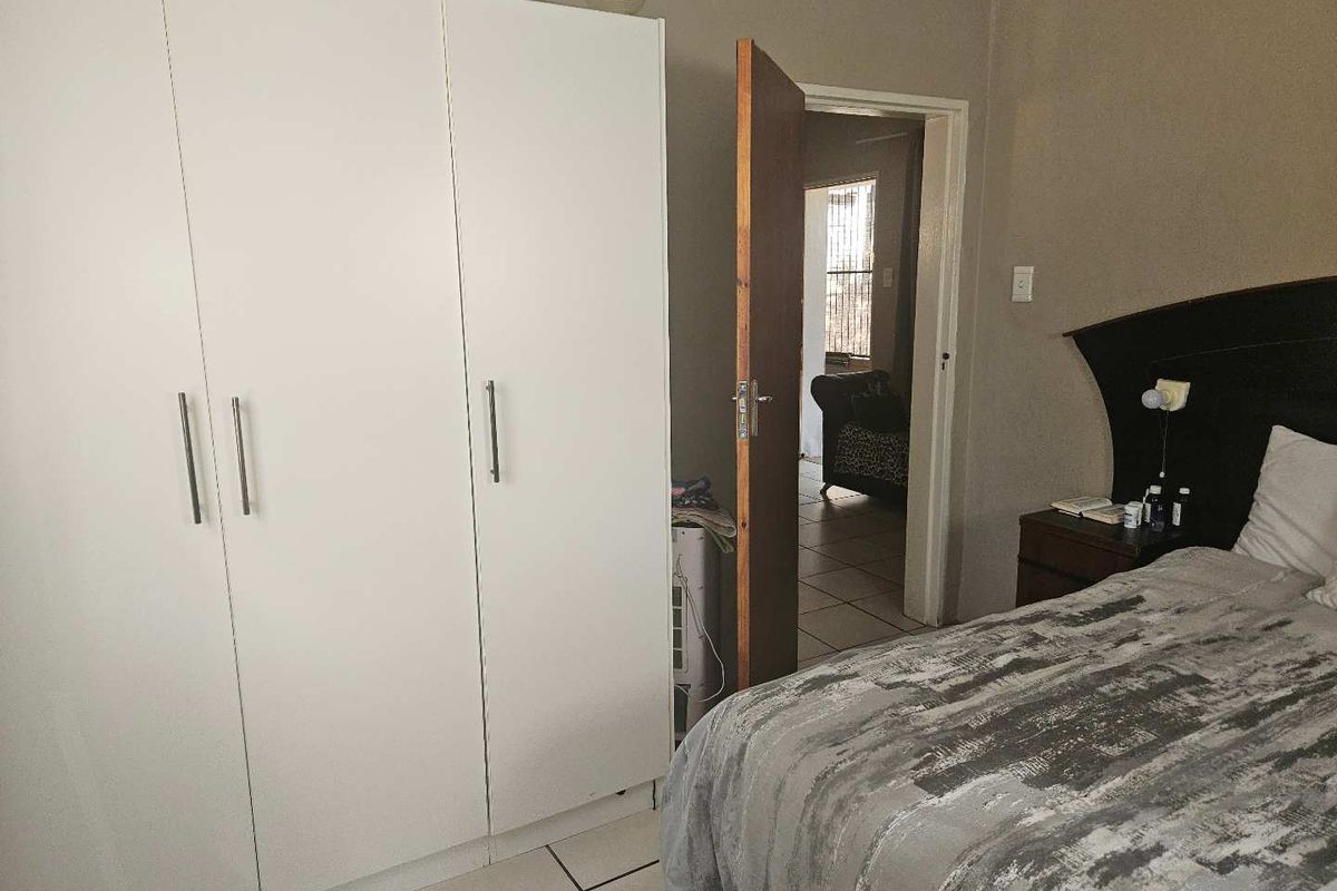 A bedroom featuring tiled flooring and a white built-in wardrobe, with an open doorway leading to an adjacent living space.