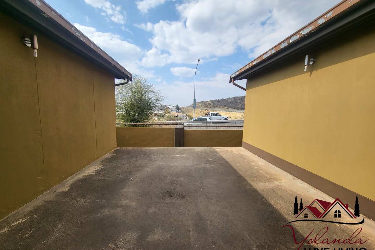 An exterior rear view showing a concrete driveway area between two building walls with visible wear to the roof eaves and surface.