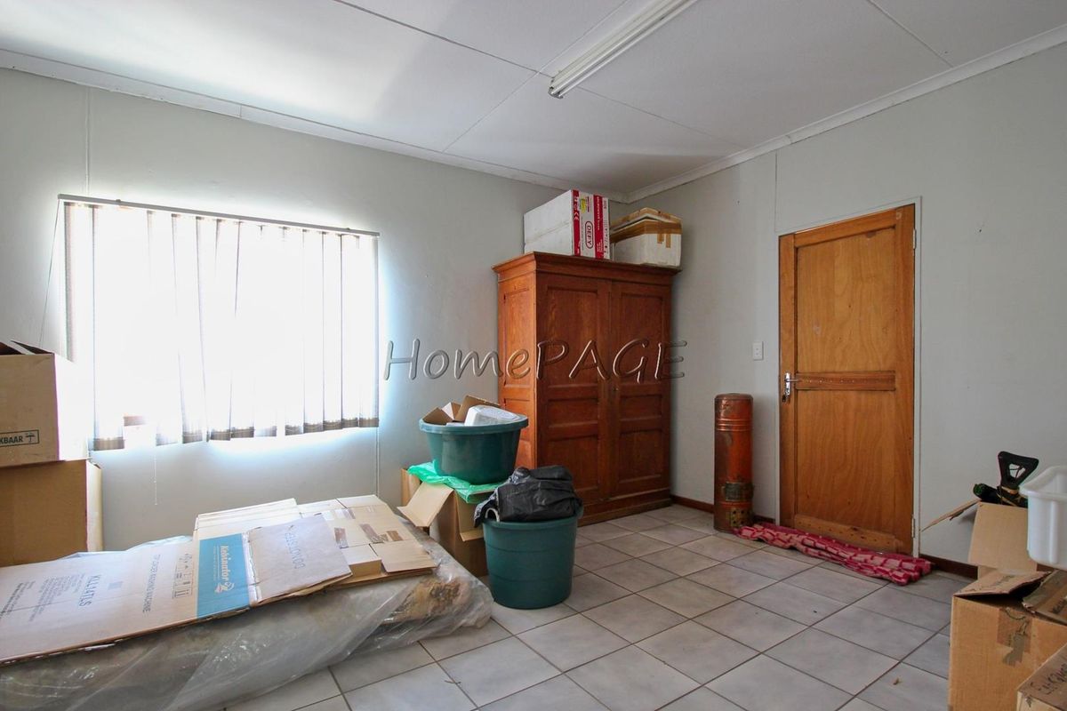 A functional utility room or bedroom featuring tiled flooring, vertical blinds, and a wooden door, currently used for storage.