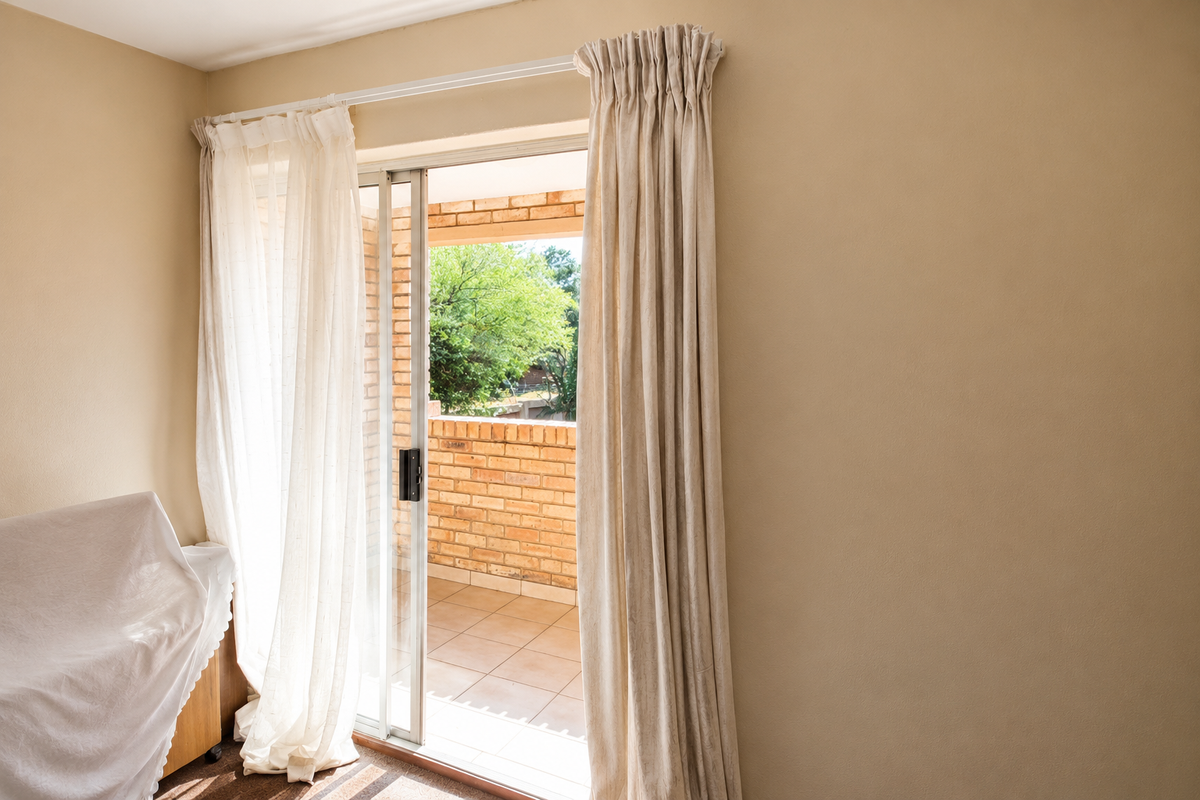 A bright bedroom featuring a sliding glass door that opens onto a private balcony with brick wall detailing.