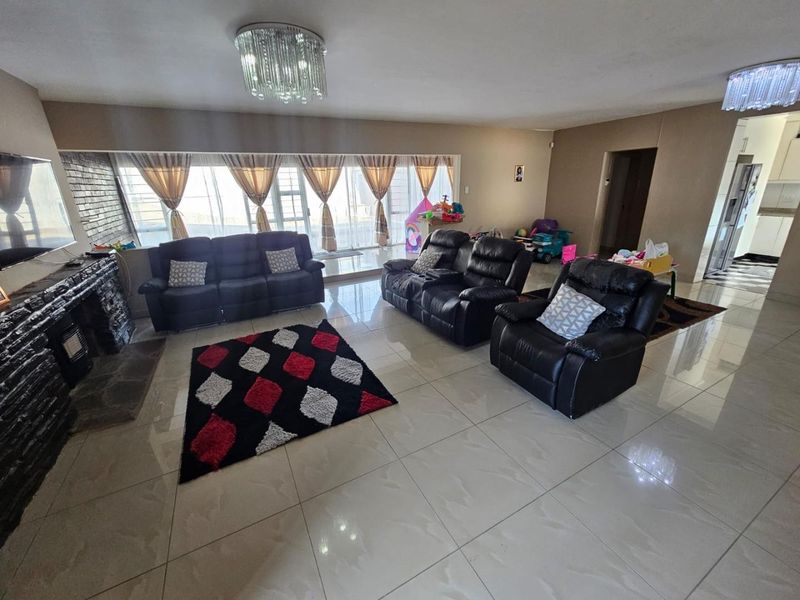 Spacious living room featuring large format floor tiles, a stone-clad fireplace, and elegant crystal chandeliers, with direct access to the outdoor area.