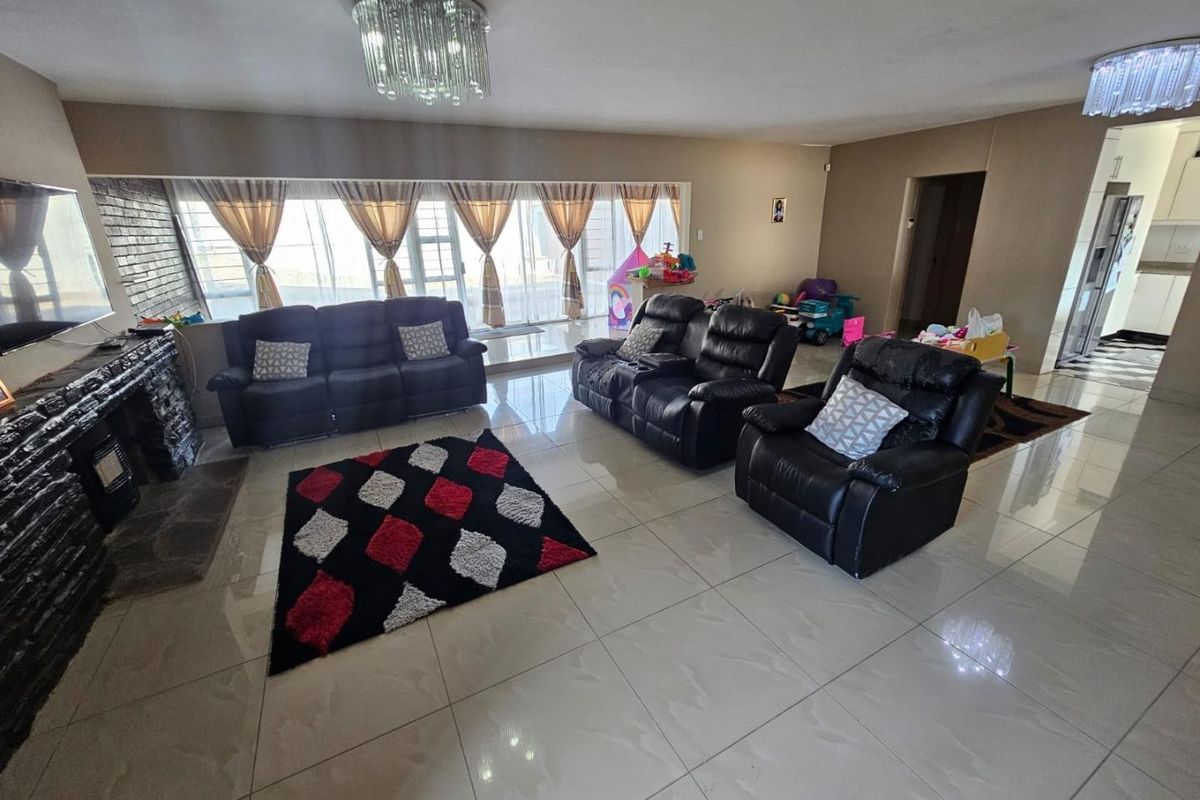 Spacious living room featuring large format floor tiles, a stone-clad fireplace, and elegant crystal chandeliers, with direct access to the outdoor area.
