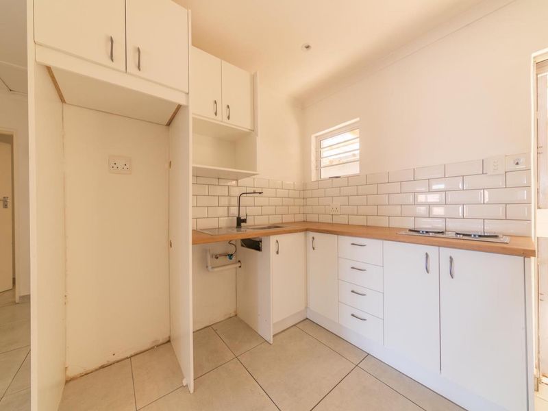 A compact, modern-style kitchen featuring white cabinetry, subway tile backsplash, wood-look countertops, and a built-in hob, presented in a clean, empty space.