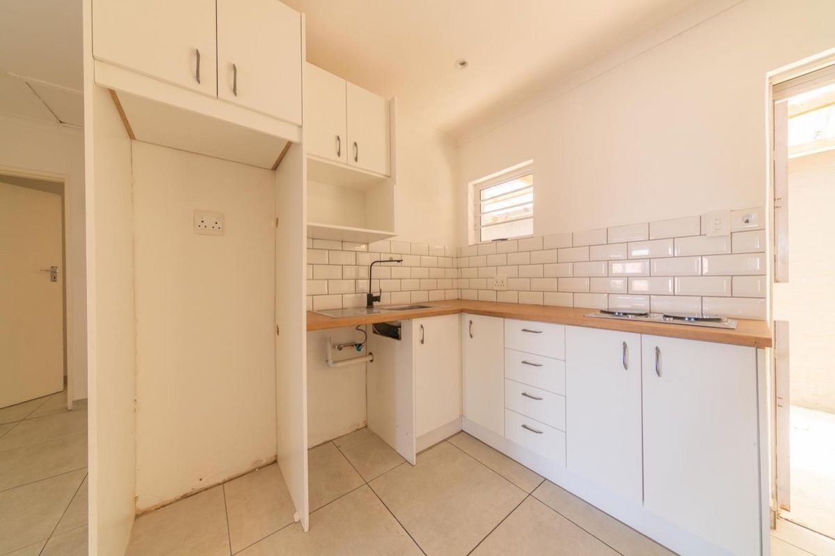 A compact, modern-style kitchen featuring white cabinetry, subway tile backsplash, wood-look countertops, and a built-in hob, presented in a clean, empty space.