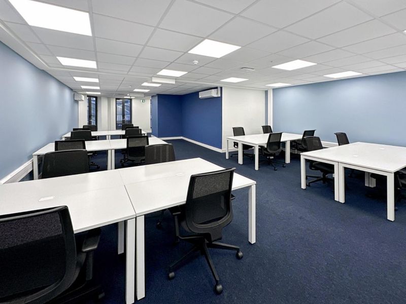 A modern, well-lit open-plan office space featuring a suspended ceiling with recessed LED panels, blue accent walls, and carpeted flooring.