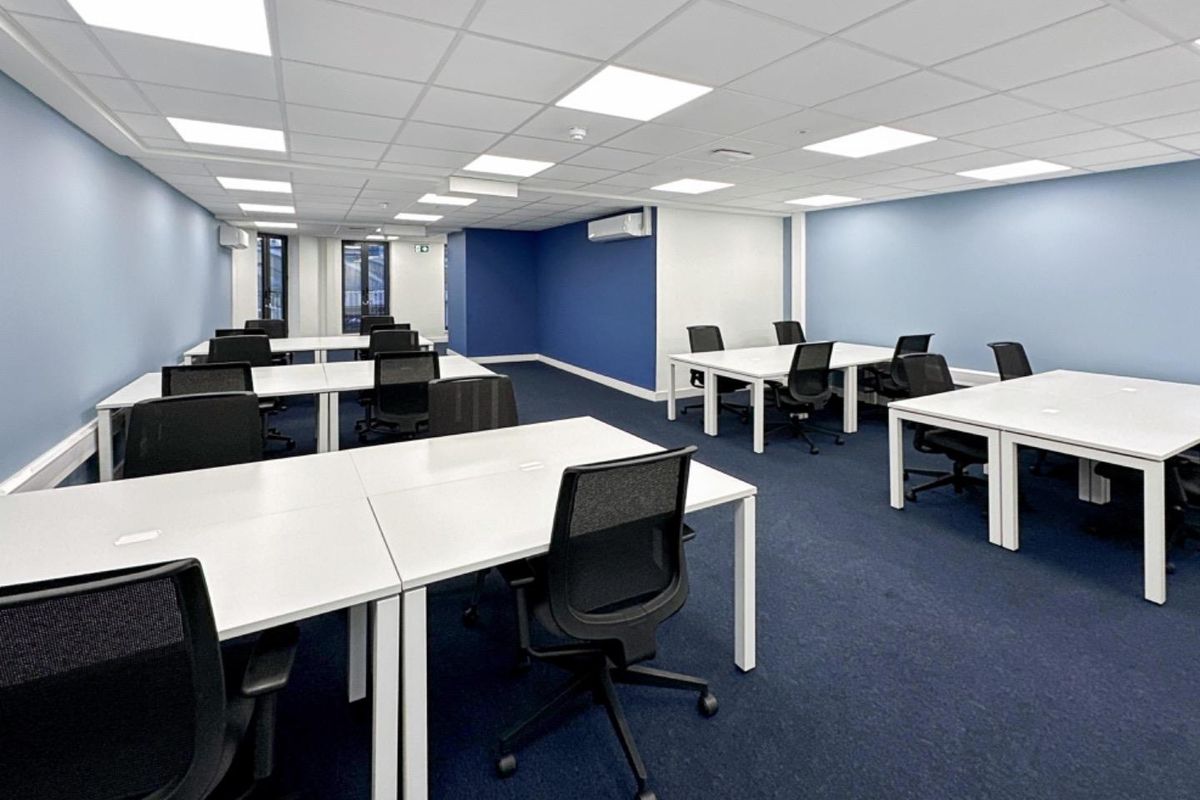 A modern, well-lit open-plan office space featuring a suspended ceiling with recessed LED panels, blue accent walls, and carpeted flooring.