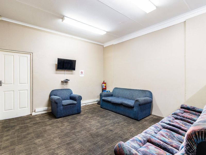A functional living area featuring carpeted flooring, neutral wall finishes, and overhead fluorescent lighting, suitable for a casual lounge or waiting space.