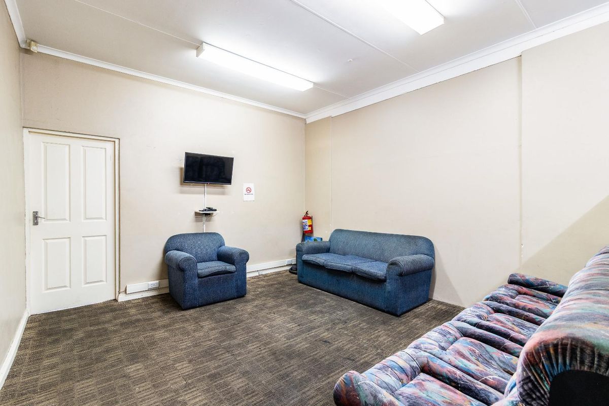A functional living area featuring carpeted flooring, neutral wall finishes, and overhead fluorescent lighting, suitable for a casual lounge or waiting space.