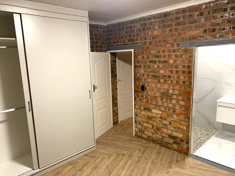 Bedroom featuring exposed brick walls, modern laminate flooring, and a large built-in wardrobe with direct access to an en-suite bathroom.