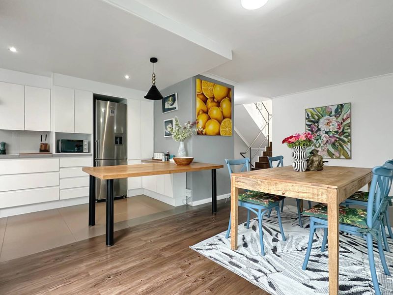 Modern open-plan kitchen and dining area featuring sleek white cabinetry, contrasting wood-look flooring, and a staircase leading to the upper level.
