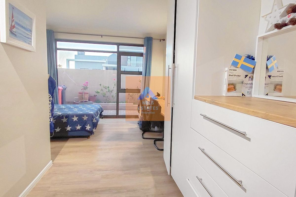 A bright bedroom featuring modern laminate flooring, built-in cupboards, and a large sliding glass door providing access to an outdoor patio area.