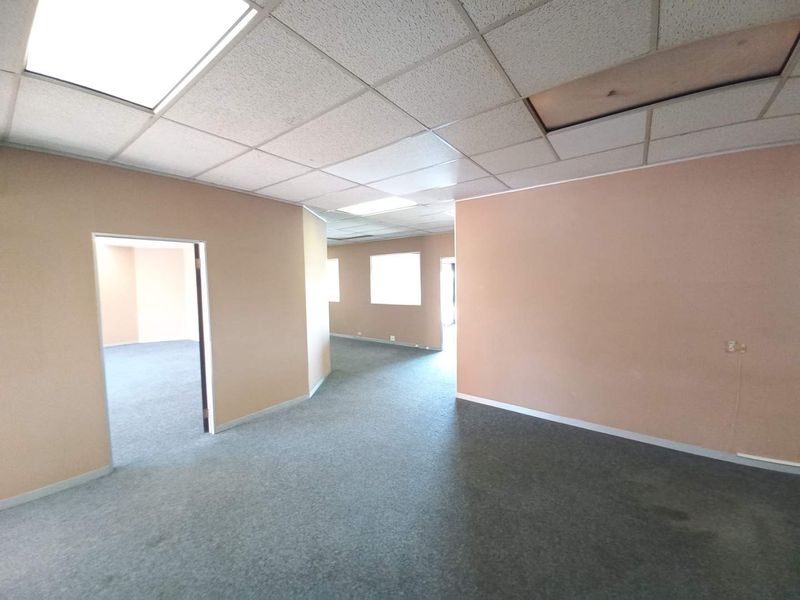 An open-plan office space featuring a suspended acoustic ceiling, grey carpeting, and neutral wall finishes, offering a flexible layout for professional use.