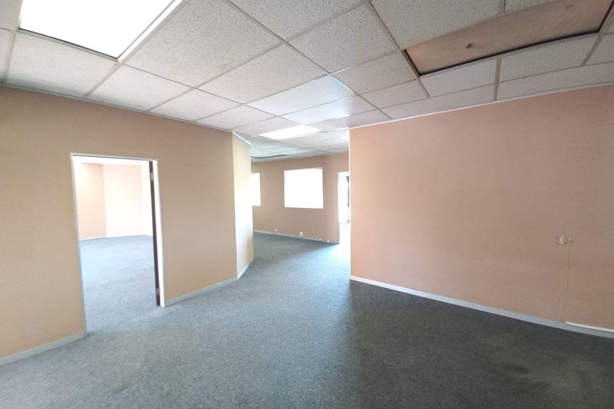 An open-plan office space featuring a suspended acoustic ceiling, grey carpeting, and neutral wall finishes, offering a flexible layout for professional use.