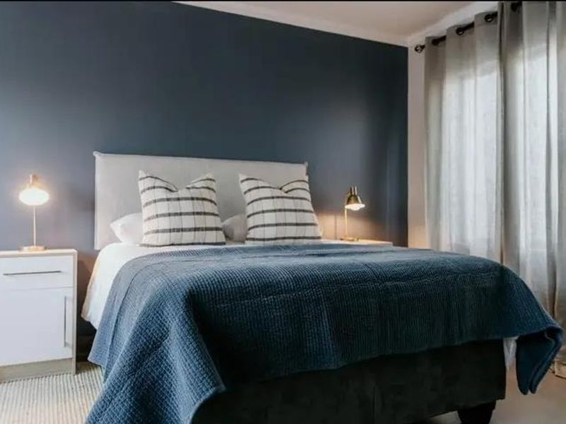 A well-presented bedroom featuring a dark blue accent wall and large windows with fitted curtain tracks.