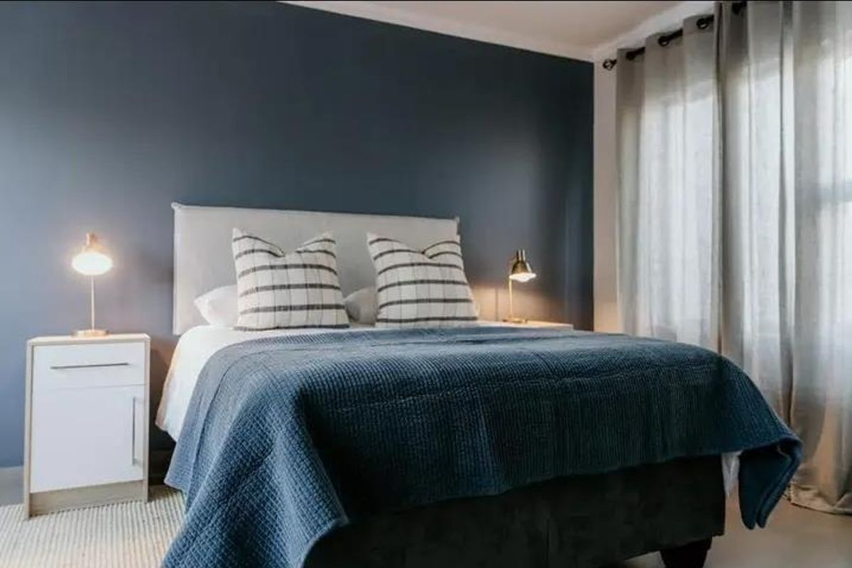 A well-presented bedroom featuring a dark blue accent wall and large windows with fitted curtain tracks.