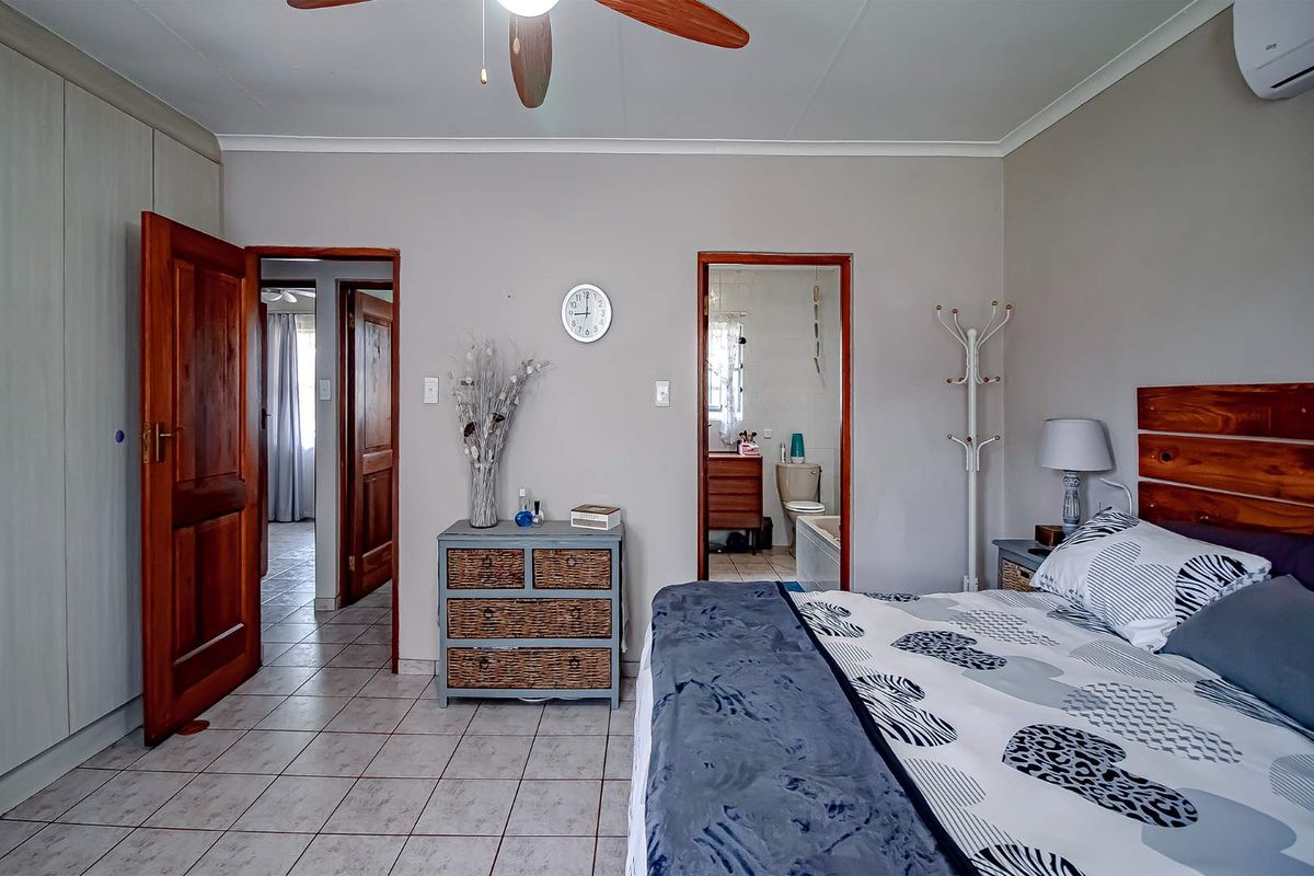A bedroom featuring tiled flooring, built-in cupboards, a ceiling fan, and an en-suite bathroom.