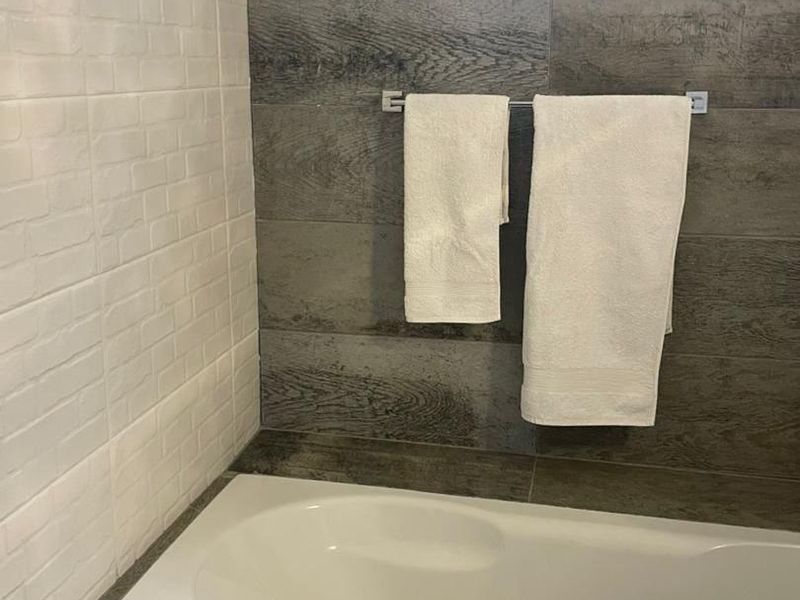 A modern bathroom featuring a built-in bathtub with contrasting white subway and wood-look tile finishes, complemented by a functional towel rail.