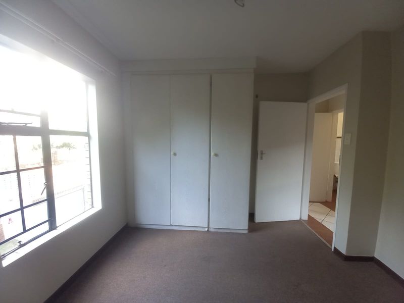An empty bedroom featuring built-in cupboards, neutral wall finishes, and a large window allowing natural light.