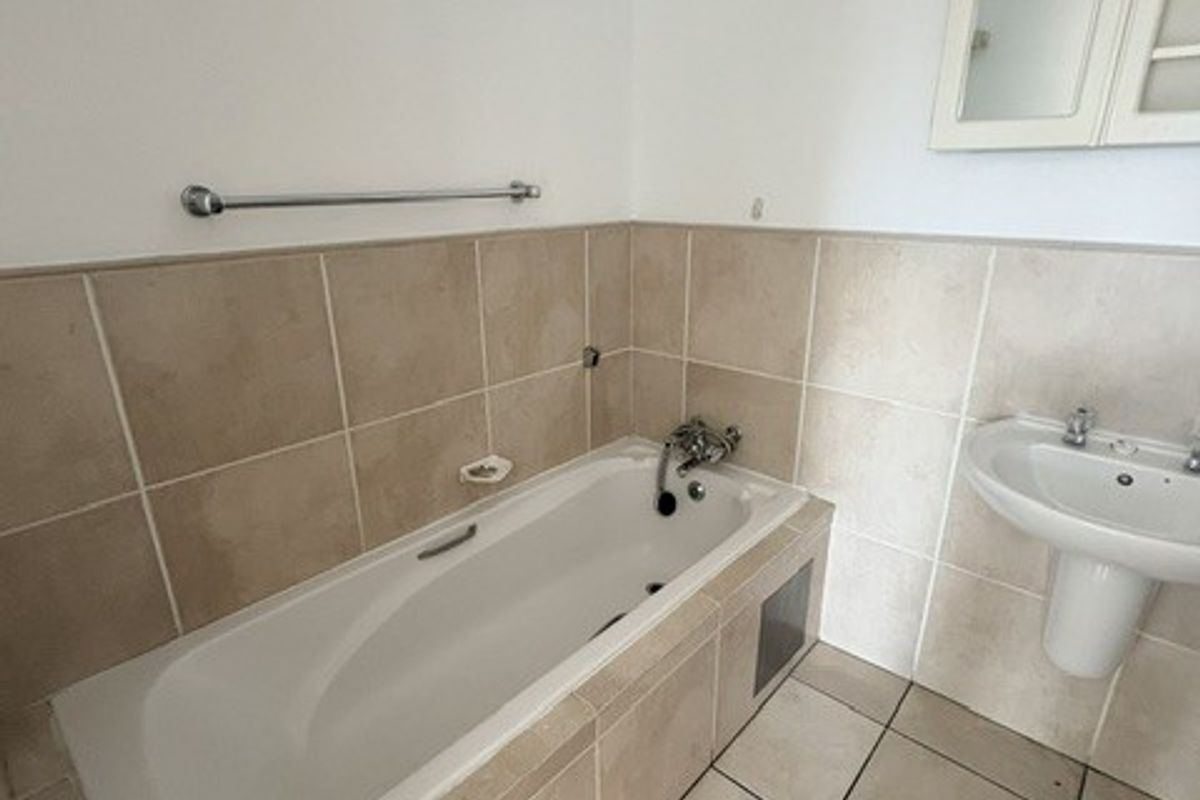 A functional bathroom featuring a built-in bathtub, pedestal basin, and neutral wall and floor tiling.