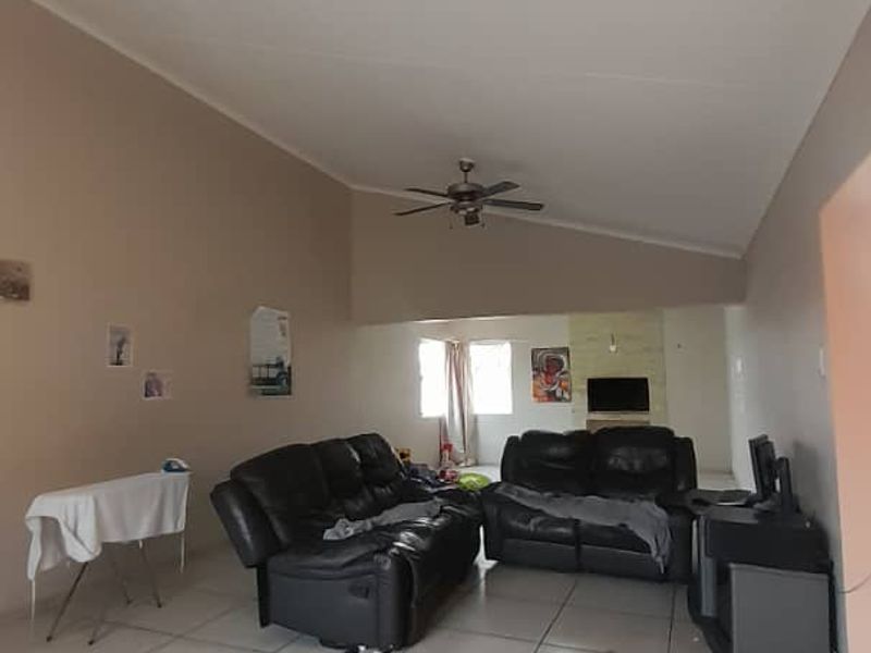 Spacious living room featuring vaulted ceilings, a ceiling fan, and neutral tiled flooring, offering a versatile layout for comfortable family living.