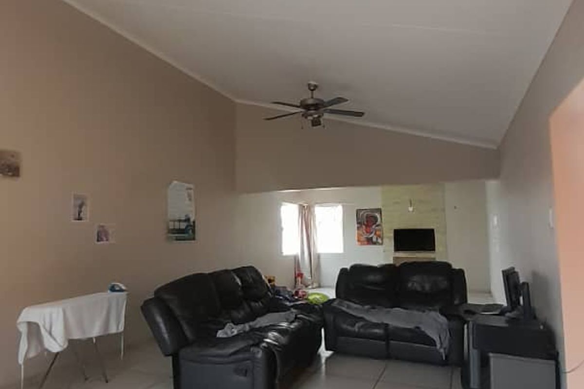 Spacious living room featuring vaulted ceilings, a ceiling fan, and neutral tiled flooring, offering a versatile layout for comfortable family living.