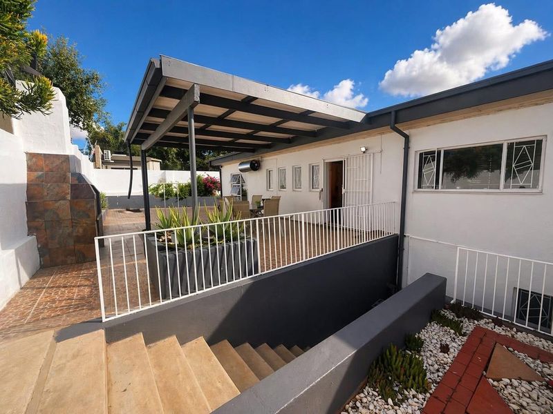 A well-maintained covered patio area featuring a built-in braai, metal balustrades, and direct access to the home via a secure door.