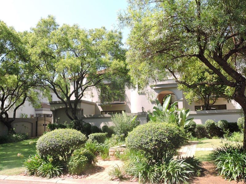Front view of a multi-story residential property featuring a landscaped garden, paved walkway, and secure boundary wall with gated access.