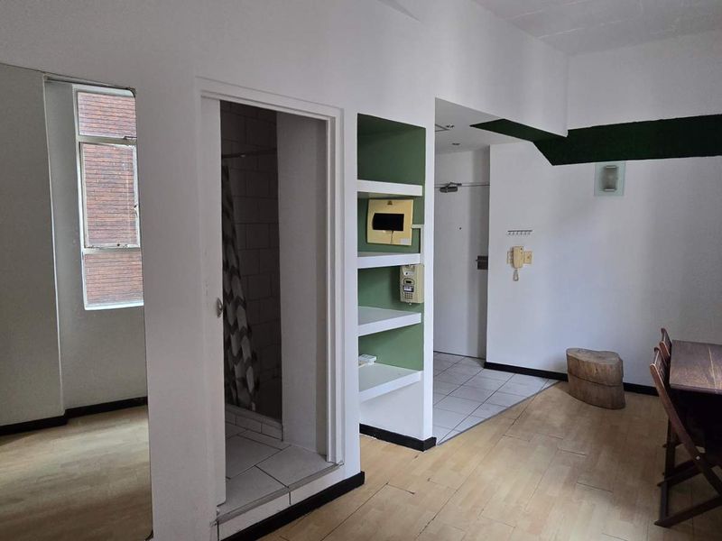 Open plan living area featuring laminate flooring, built-in shelving, and an integrated intercom system, with an adjacent tiled bathroom entrance.