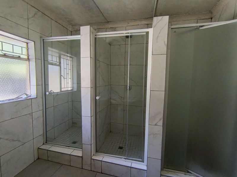 A functional bathroom featuring multiple tiled shower enclosures with glass doors and tiled finishes throughout.
